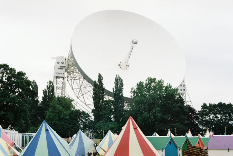 a large satellite dish sitting on top of a hill near some umbrellas