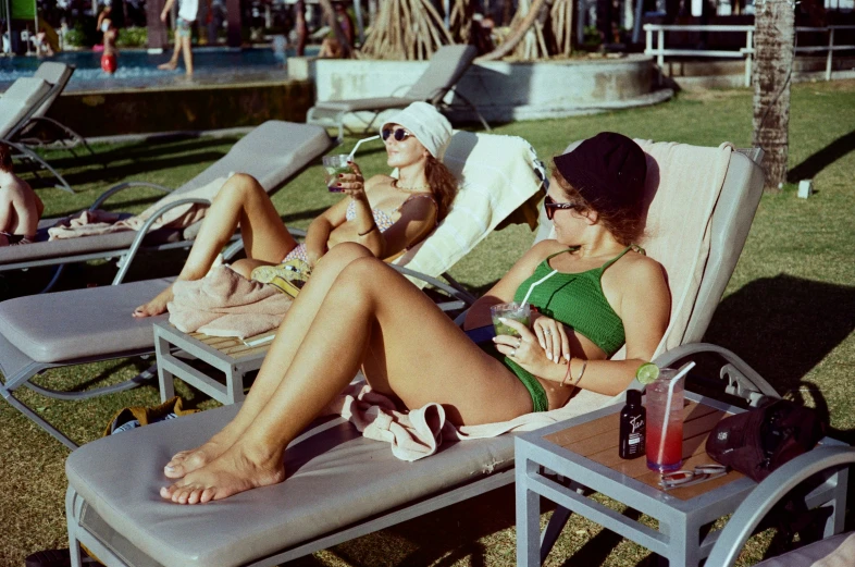 a woman in a bathing suit lies on a lawn chair while another woman uses her cell phone