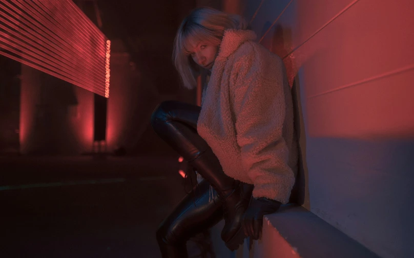 a woman leaning against the wall in front of an orange light