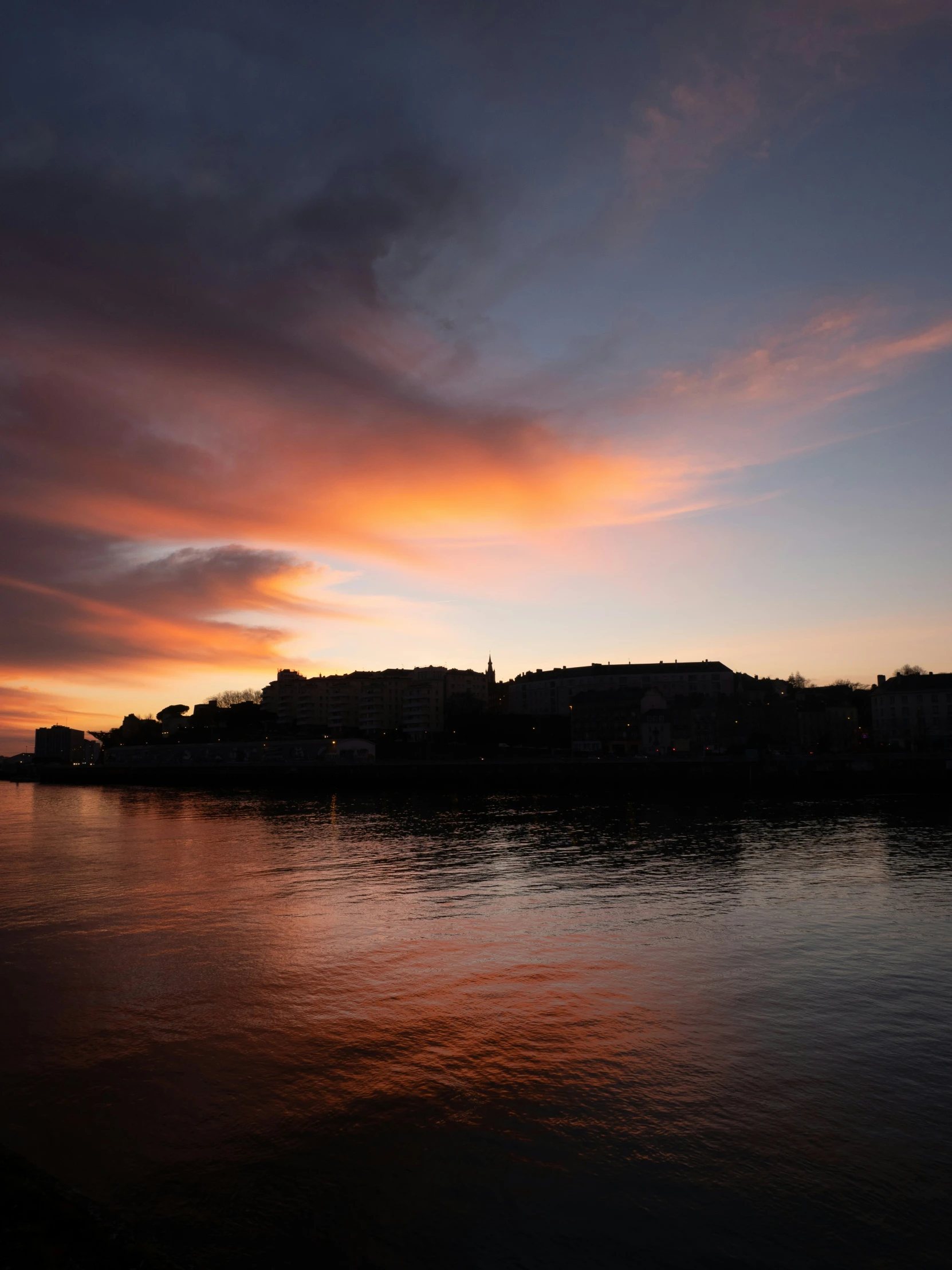 the silhouette of a city is pictured during sunset over water