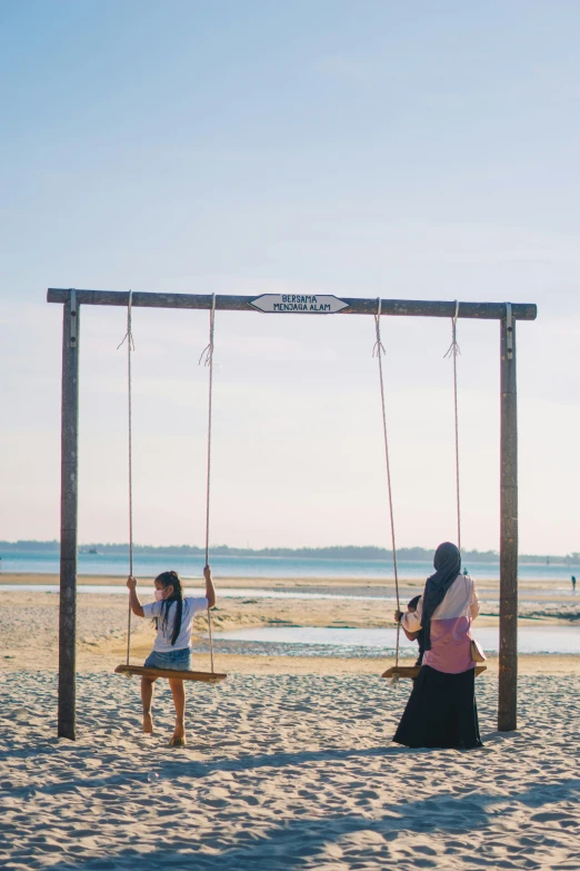 the girls are playing on the swings at the beach