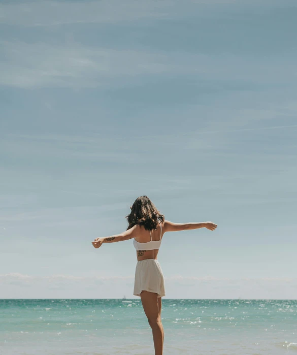 a woman is on the beach in a white bathing suit and she has one hand up