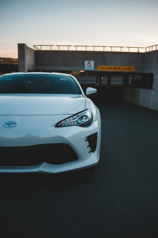 a white toyota sports car sits in front of a bridge