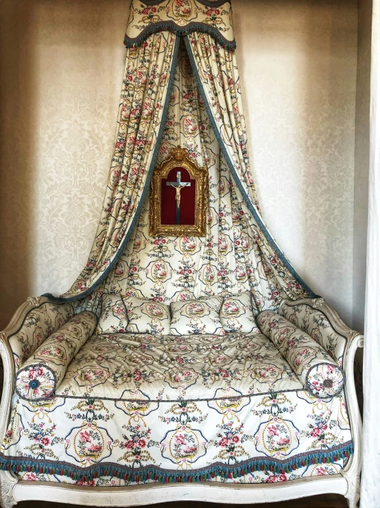 a bed covered in a floral print with a gold cross on top