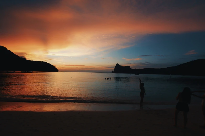 some people are standing on the beach at sunset