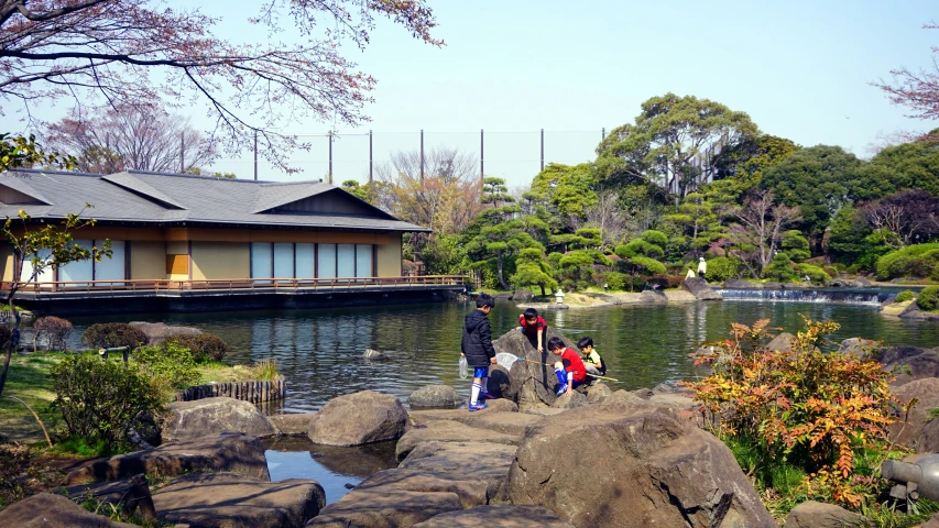 people on rocks looking at a house by the water