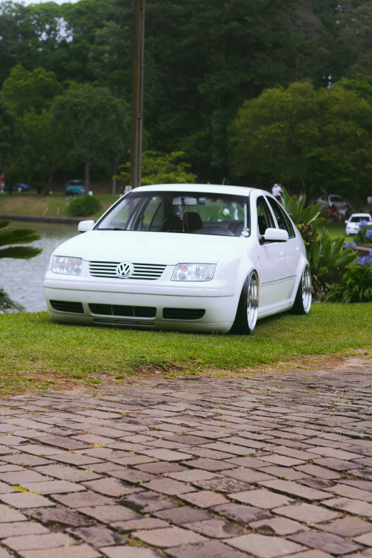 a white car parked next to a lake and brick road