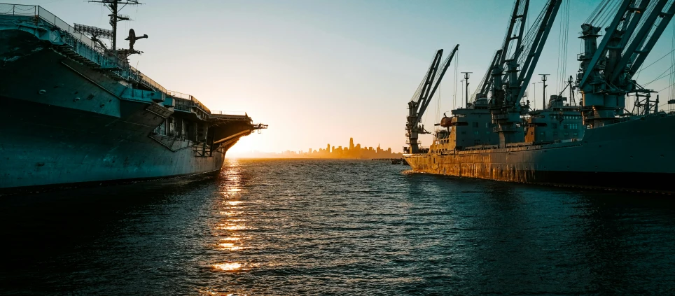 the sun rises between two ships in a harbor