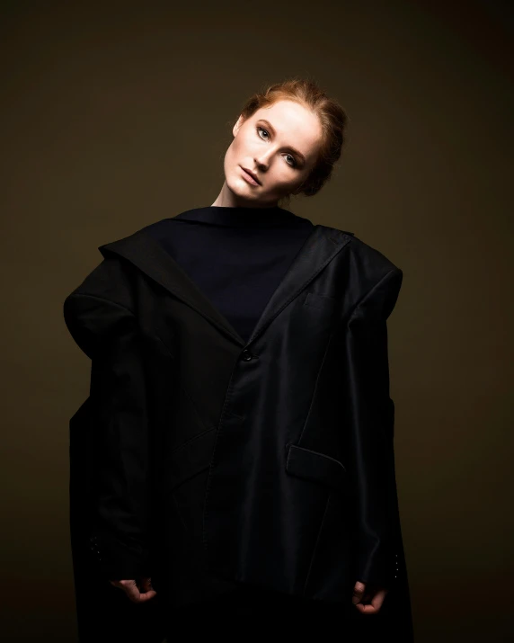 a woman wearing a black coat standing against a wall