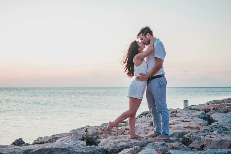 a couple is kissing on rocks by the water