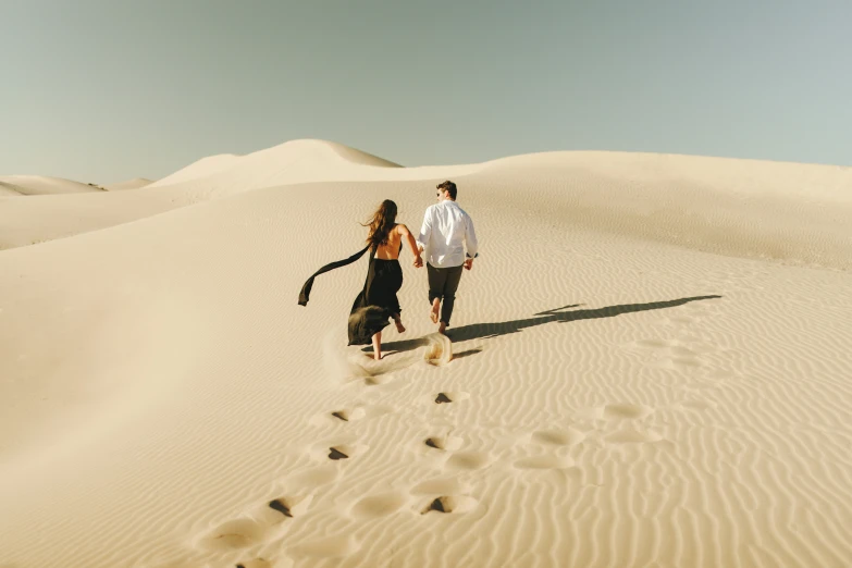 a man and woman running down a sand dune