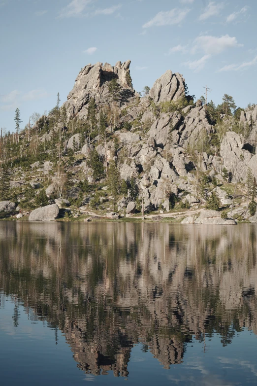 rocks reflect the sky near water with the reflection of pine trees