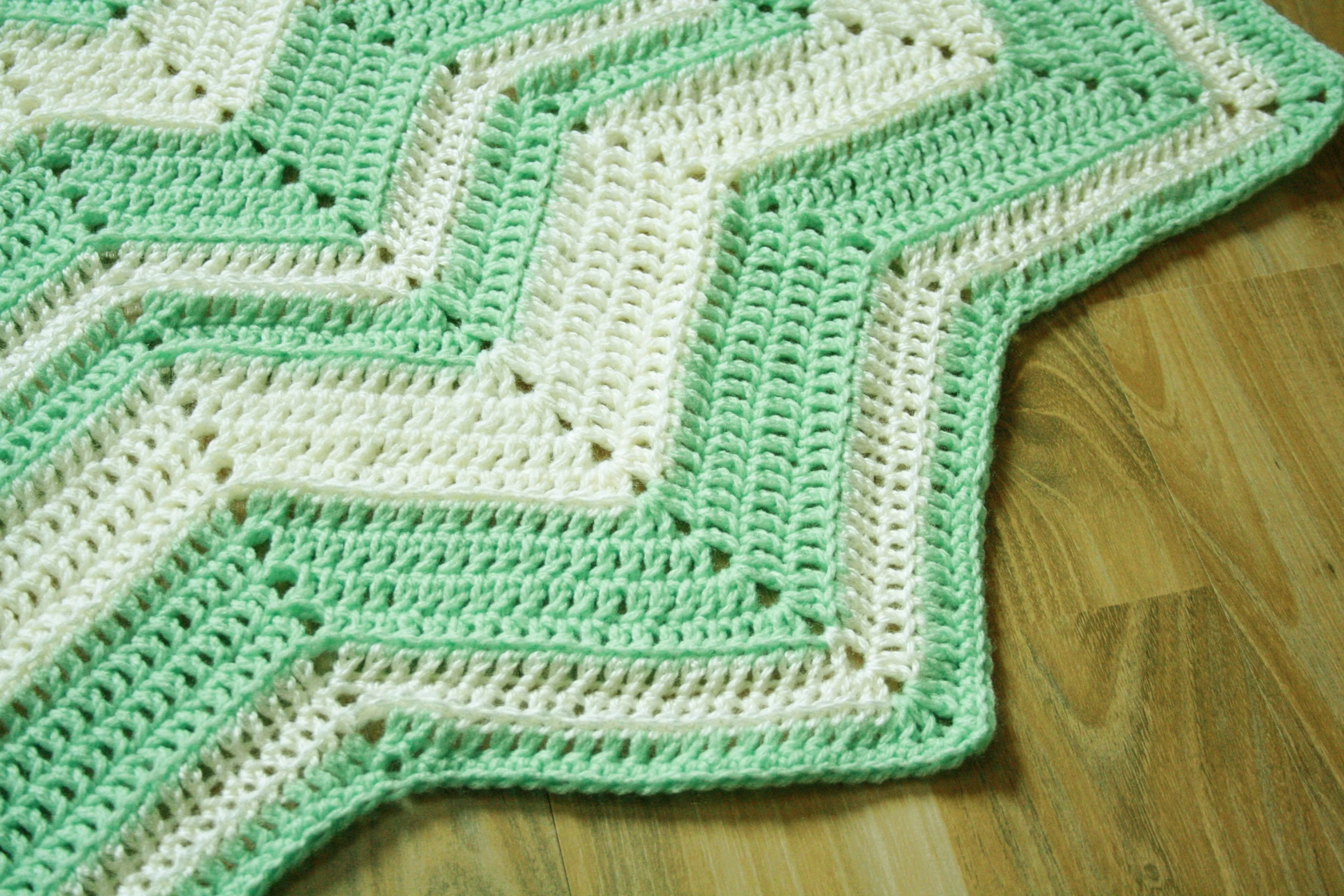 a green and white knitted blanket sits on the floor