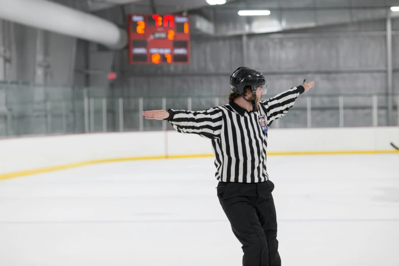 a hockey referee on a skating rink holding his hands out in a big open area