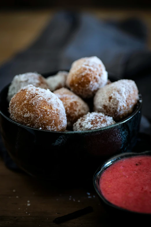 a bowl filled with powdered sugar donuts next to sauce