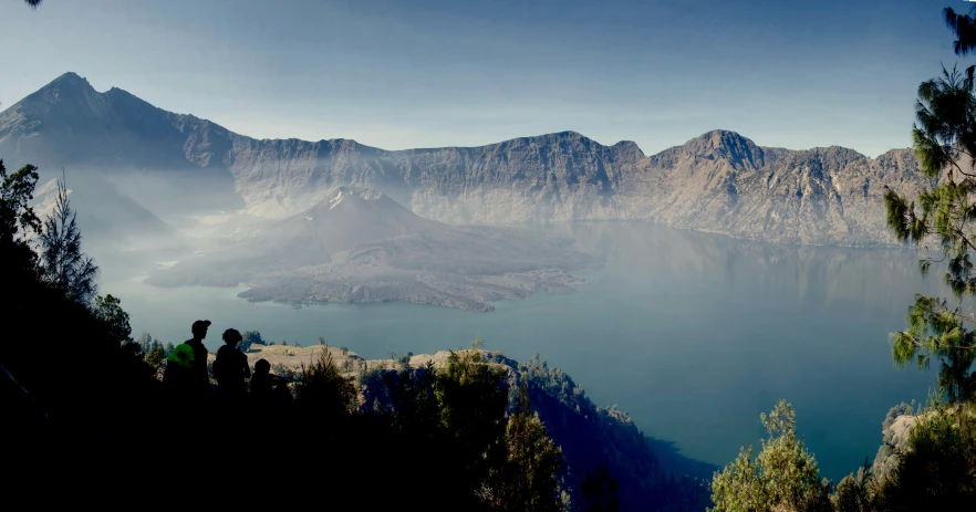 people overlooking a lake surrounded by mountains and trees