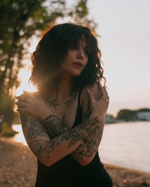 a woman with tattoos and a black dress by the water