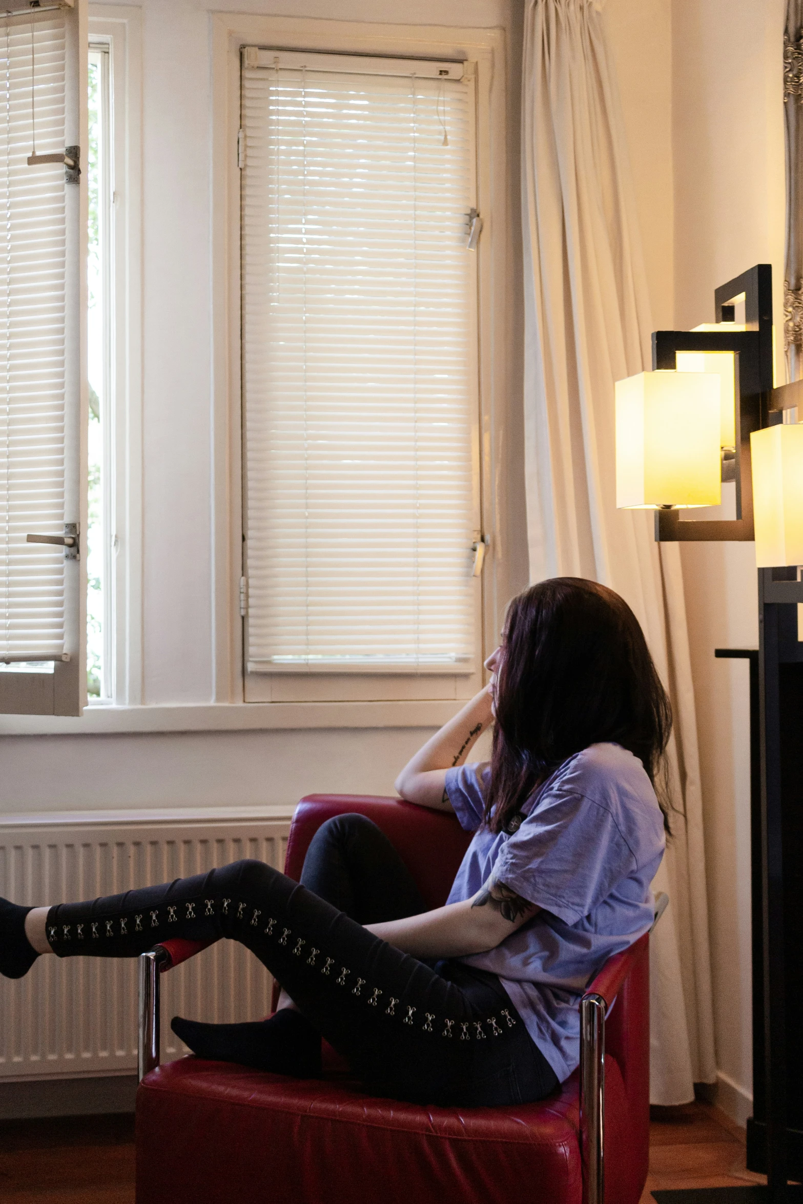 a woman sits on a red chair and stares out the window