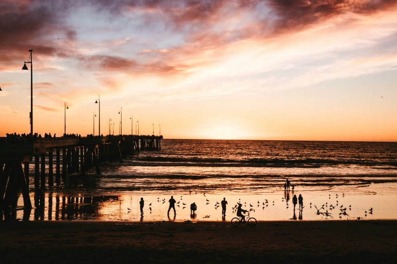 people are standing near the water at sunset