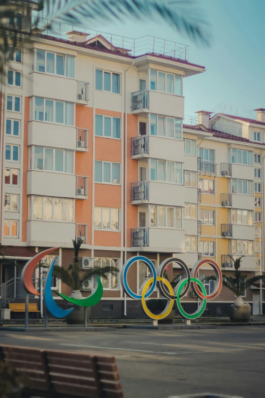 the olympic rings sitting in front of buildings on a sunny day