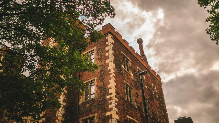 a red brick building with some trees and cloudy skies