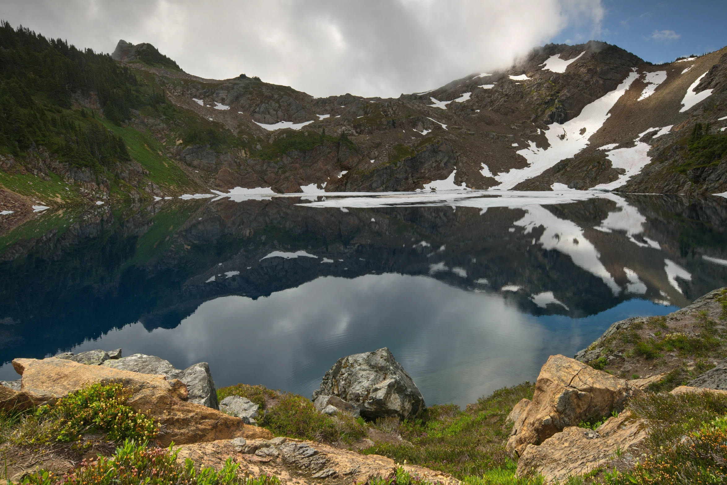 an alpine lake with some snow and clouds