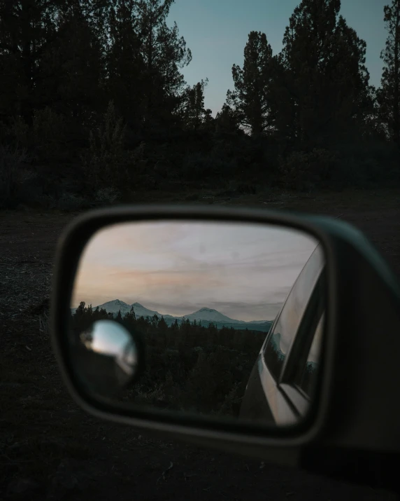 the rear view mirror on a vehicle in front of a dusk sky