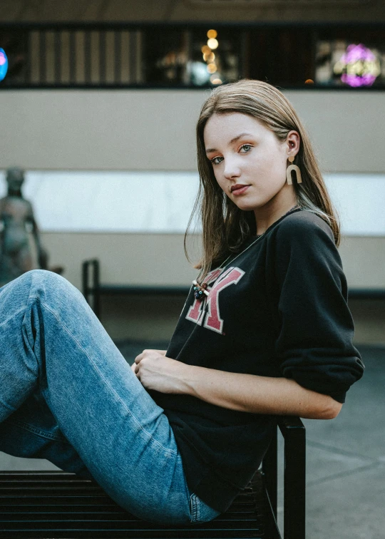 a girl in jeans and black shirt sitting on a bench