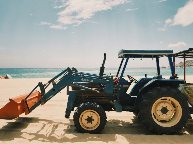 an tractor parked on the beach, with its loader extended