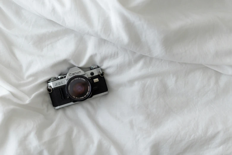 an old camera laying on a bed with a white cover