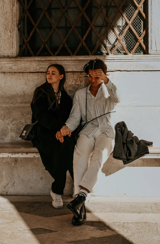 two people sit on a stone bench, one on her phone