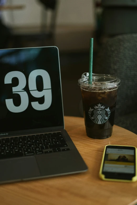 a cup of coffee and cellphone with a laptop on a table