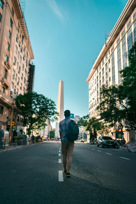 a man is walking across the street toward a tall obelisk