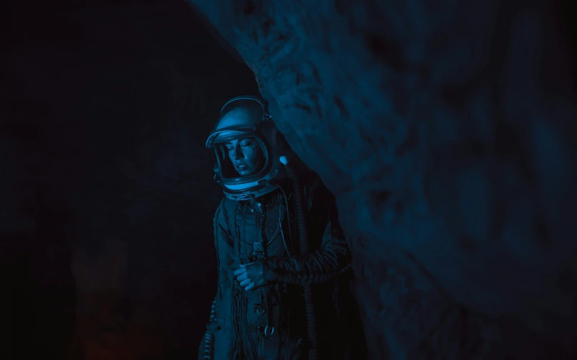 a man wearing a spacesuit standing in front of a cave