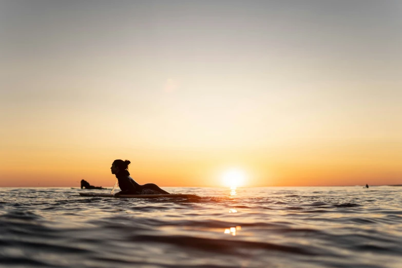 a silhouette of a person riding a surfboard at sunset