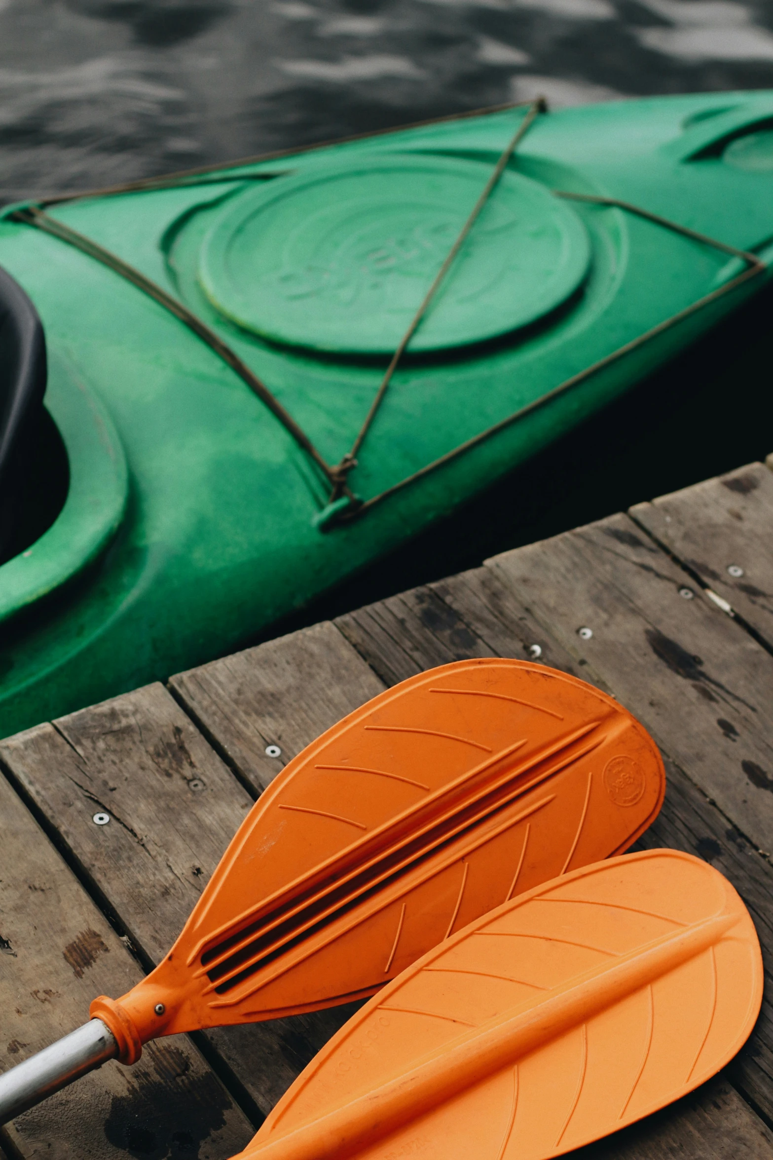 a single orange kayak sits on the edge of a dock with paddles