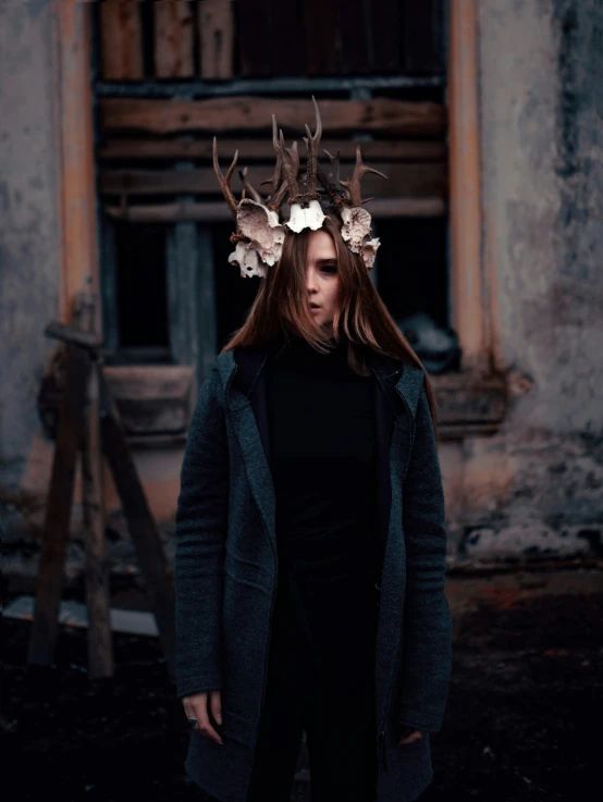 a woman with antlers standing in front of an abandoned building