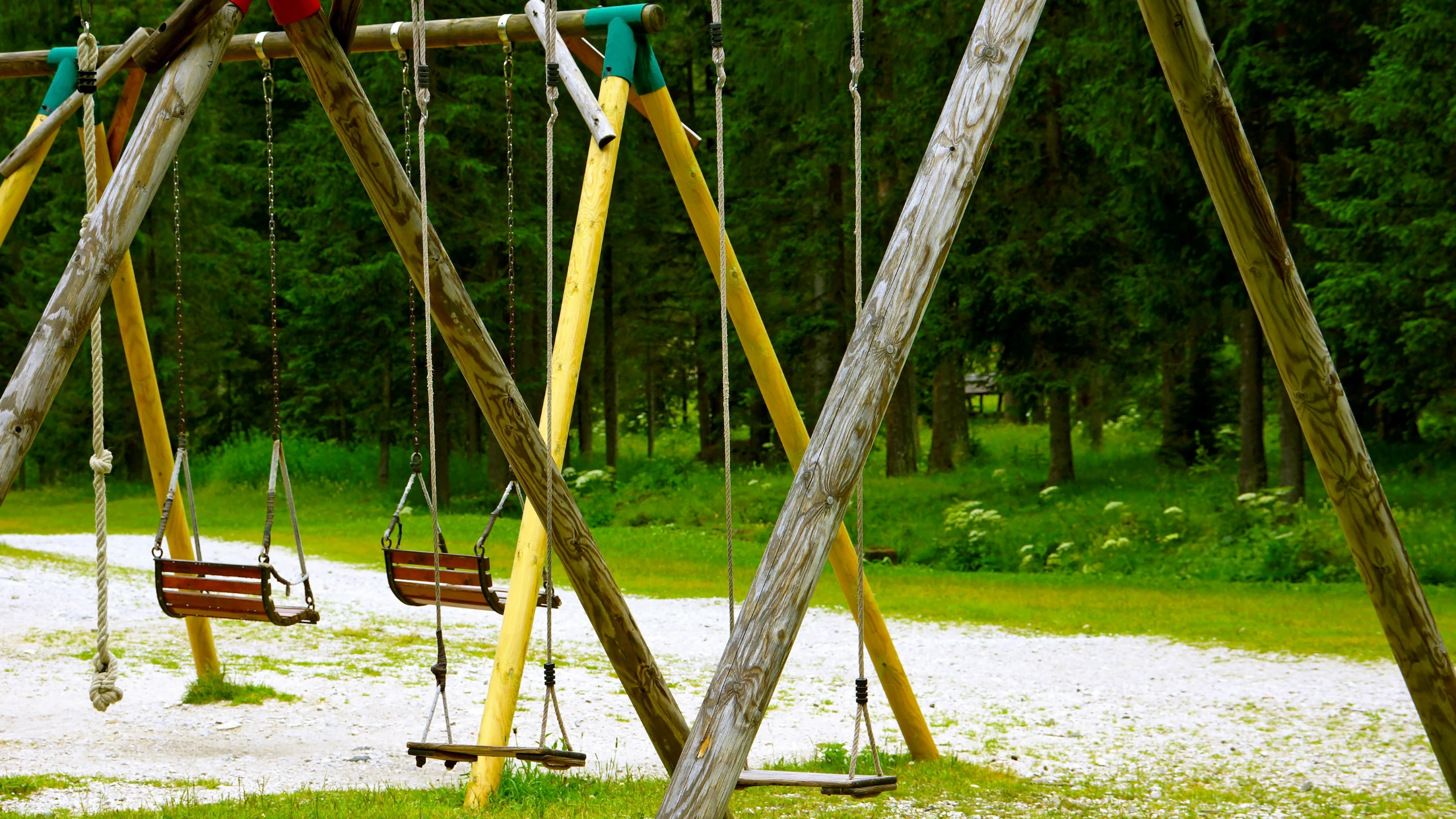 three wooden swings on the ground near trees