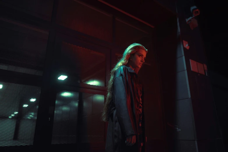 a girl wearing a coat standing outside a building at night