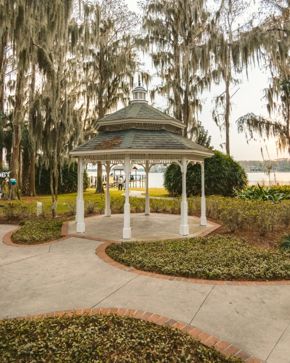 a white gazebo with lots of moss and trees behind it