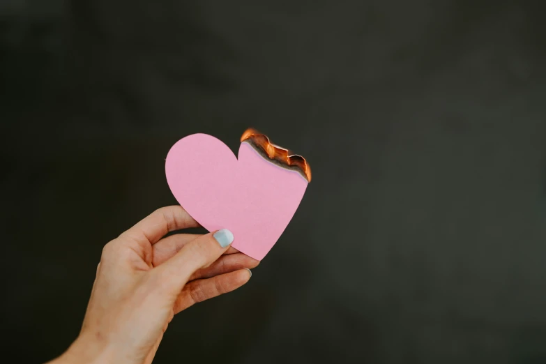 a person holding a paper heart over a black background