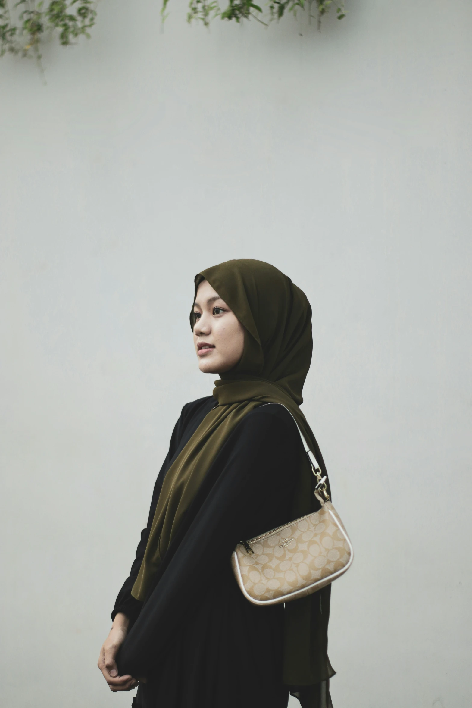 a woman wearing a green hijab is holding a white purse