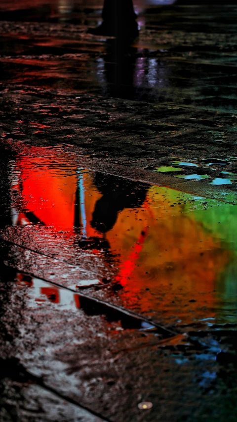 a rainbow colored umbrella is reflected in the wet rain