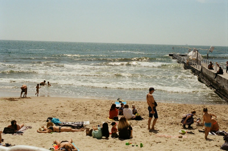 a crowd of people stand on a beach while one is wearing a black shirt and one is carrying a baby