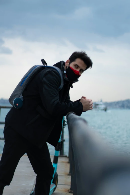 a man in black coat and red mask near the water