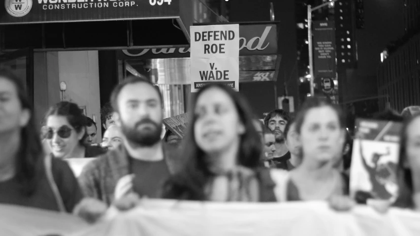 group of people sitting at table together, looking up at a sign