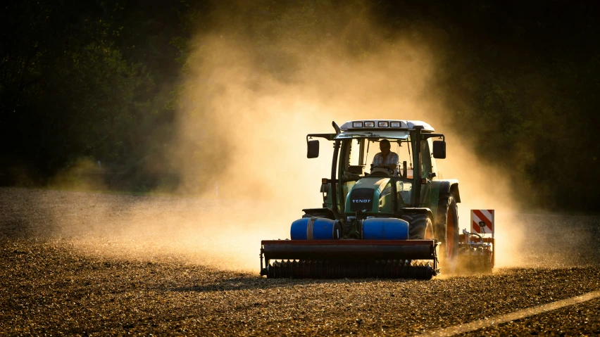 a tractor moving through the dirt with dust coming from its tires