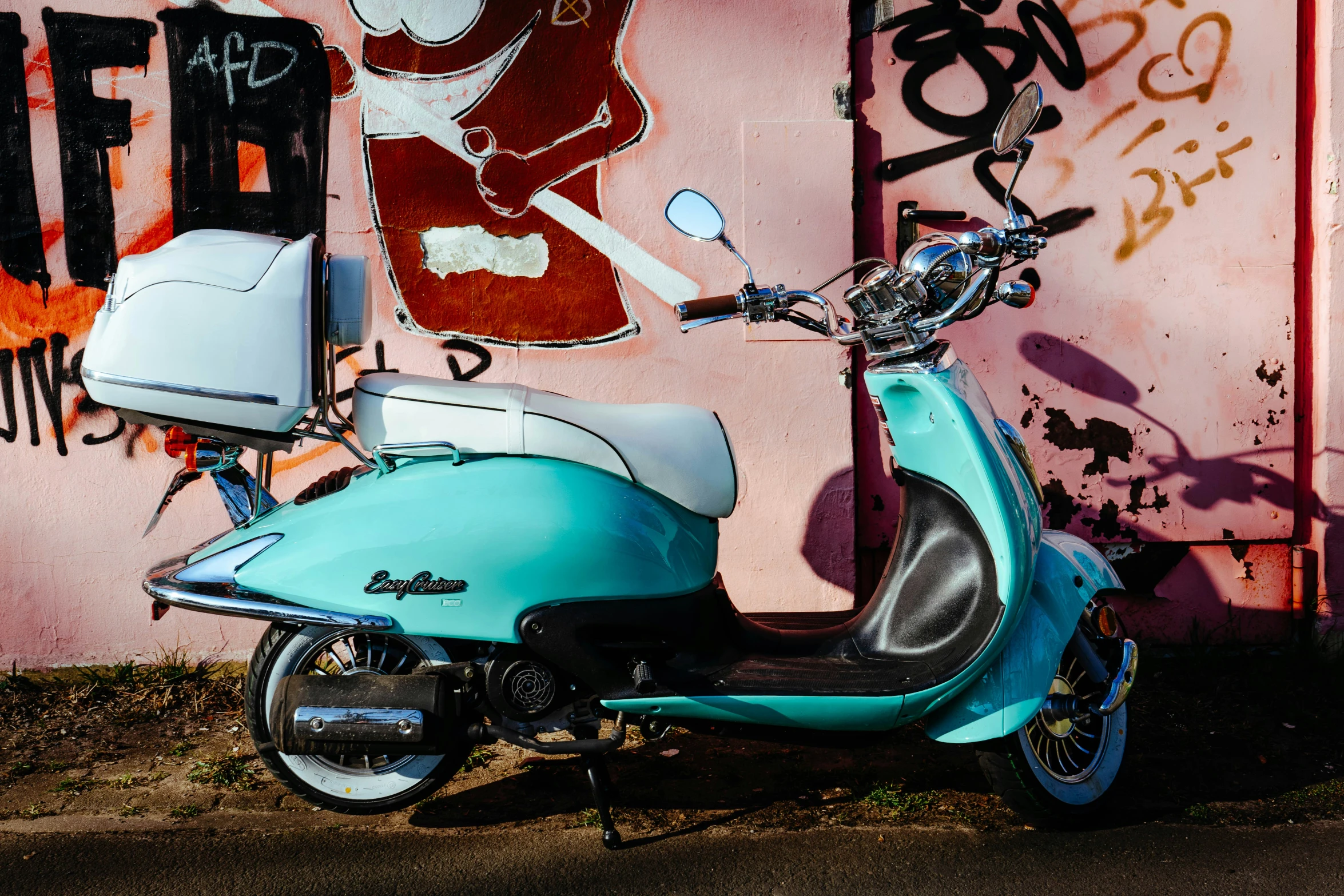 a blue motor scooter parked next to a wall with graffiti