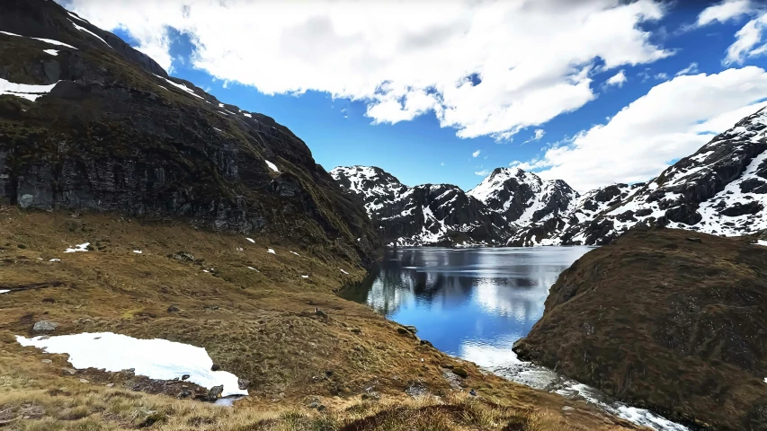 an alpine valley with snow covered mountains and a pond