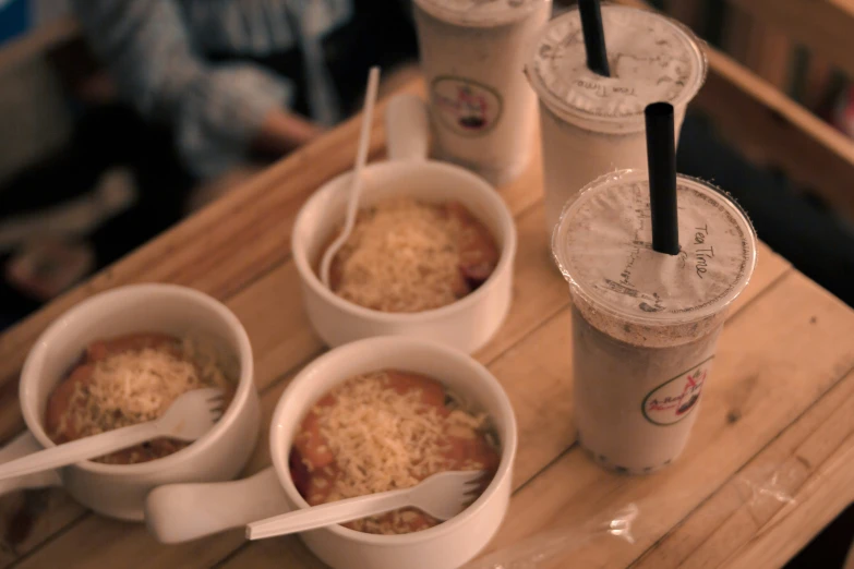 a wood table holding three drinks and cups of food